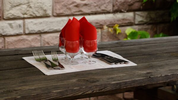 A close up photo of dark wood dining furniture in a bistro restaurant, with a white table cloth in the middle with four wine glasses decorated with red napkins and cutlery