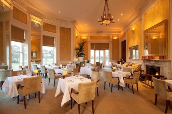 A photo of a fine dining restaurant room, with cosy upholstered restaurant chairs and restaurant tables spaced generously apart to create an ambient feel.